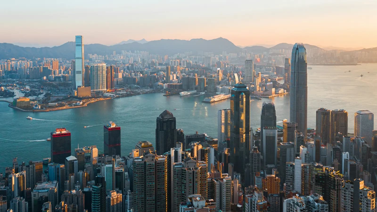 The Hong Kong skyline across Victoria Harbour, seen from above at sunrise.