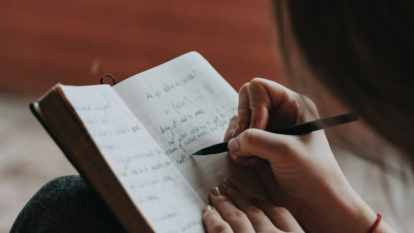 Close-up of a woman writing notes with a pen in a small hardback notebook.